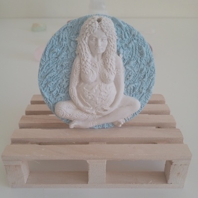 Escultura branca feminina sentada sobre disco azul em suporte de madeira clara