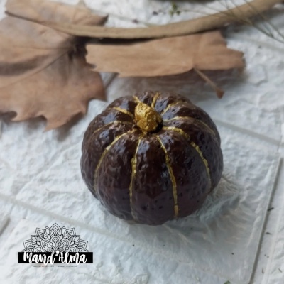 Abóbora cerâmica castanha com riscas douradas sobre base texturada e folhas secas