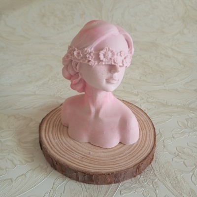 Busto feminino cor-de-rosa com banda de flores a tapar os olhos sobre base de madeira