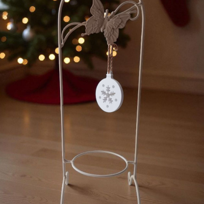 Suporte metálico branco com borboleta e enfeite de Natal pendurado.