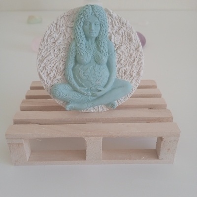 Estatueta azul clara de mulher sentada em palete de madeira.