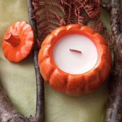 Vela em recipiente de cerâmica laranja em forma de abóbora entre ramos e folha seca
