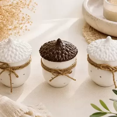 Recipientes cerâmicos em forma de bolota com tampas e cordas, decorados sobre tecido creme