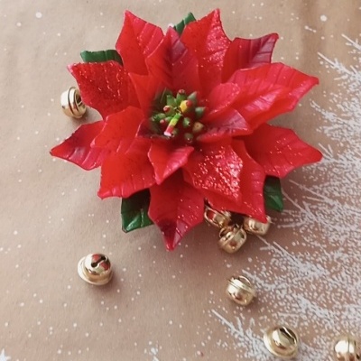 Flor de Natal vermelha artificial com pequenos sinos dourados em fundo bege com padrão de neve