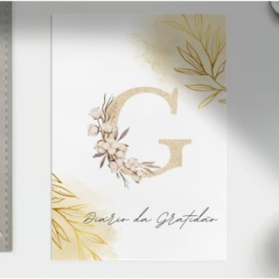 Cartão com letra G dourada e texto Diário da Gratidão junto a régua, caneta e café sobre mesa branca