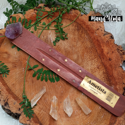 Incensário de madeira com pedra de ametista e estrelas douradas, sobre base de madeira e folhas verdes