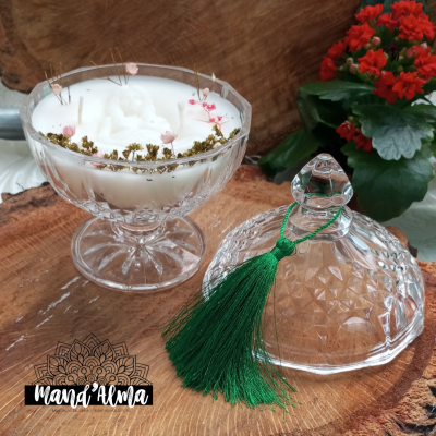 Vela branca decorativa em vidro com flores secas e tampa com tassel verde sobre madeira