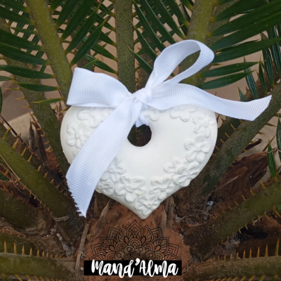 Ornamento coração branco com flores em relevo e laço branco pendurado em planta verde
