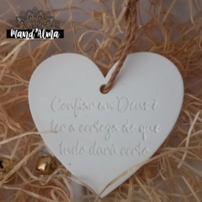 Coração decorativo branco com cordão e frase em relevo, sobre palha seca