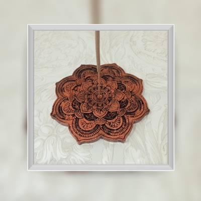 Apoio para incenso em madeira com padrão mandala preto e fundo de tecido branco floral.