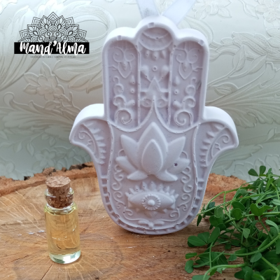 Vela branca em forma de mão de Hamsá com frasco de óleo aromático e plantas verdes