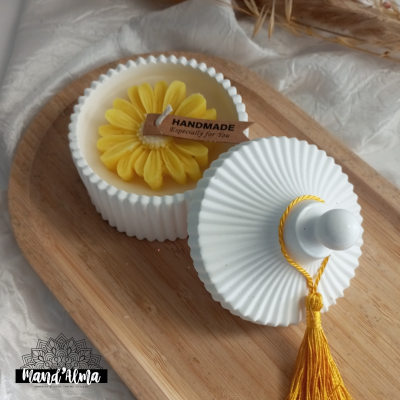 Vela amarela em forma de flor em frasco branco com tampa e etiqueta 'HANDMADE'