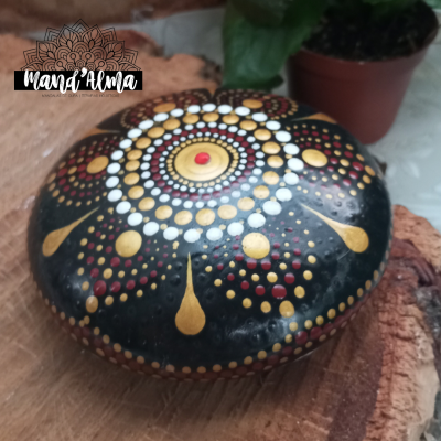 Pedra pintada com pontos coloridos sobre base de madeira ao lado de planta