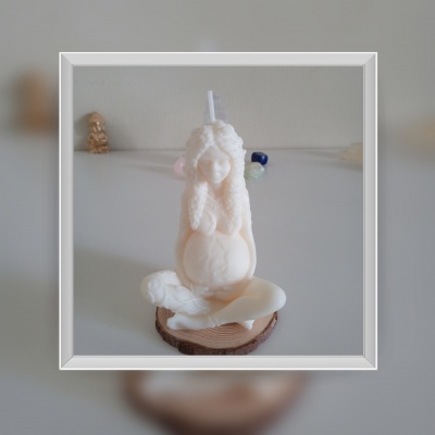 Vela branca com forma de figura humana sentada sobre base de madeira