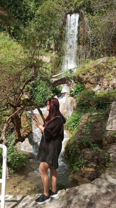Mulher de vestido preto junto a cachoeira na natureza
