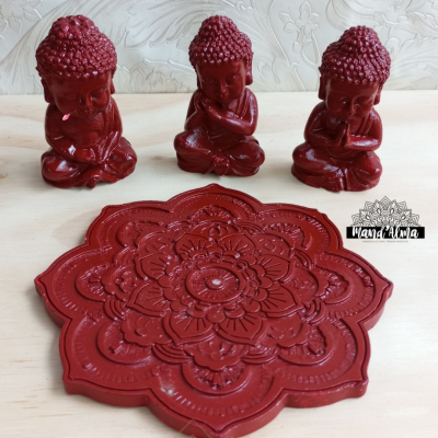 Três estatuetas vermelhas de Buda e base decorativa vermelha com padrão floral.