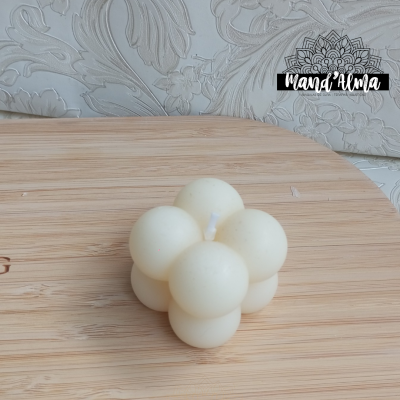 Vela branca em forma de bolhas sobre superfície de madeira clara com papel de parede floral ao fundo