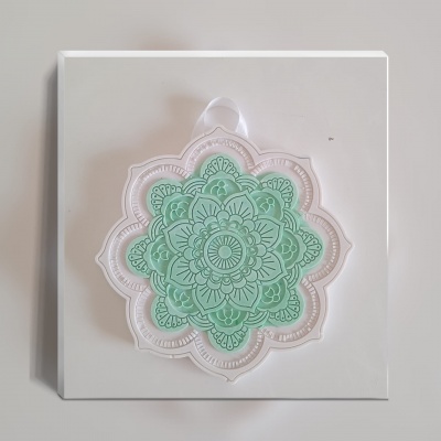 Caixa branca com decoração de mandala verde em relevo e laço branco.