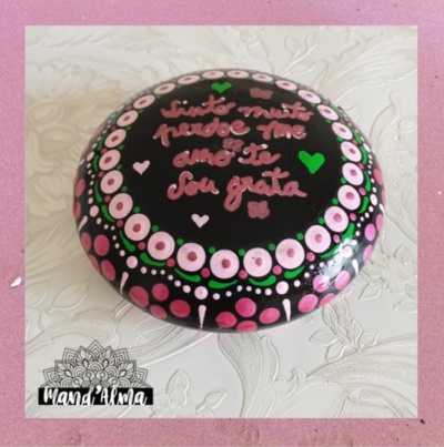 Pedra pintada à mão com padrões circulares rosa e texto em rosa sobre fundo preto