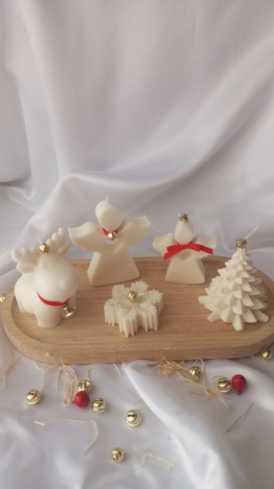 Cinco velas brancas natalícias com laços vermelhos e sinos dourados numa base de madeira com pano branco e sinos ao redor.