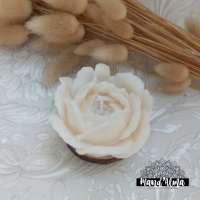 Vela branca em forma de flor com palha seca ao fundo sobre superfície branca com padrão floral