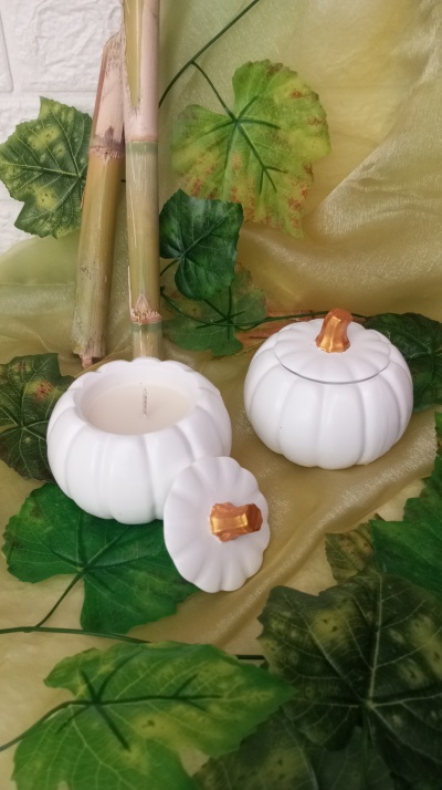 Vela decorativa branca em forma de abóbora com tampa dourada e folhas verdes artificiais