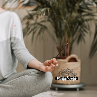 Pessoa meditando, vestindo cinza e branco, segurando incenso aceso junto a planta grande