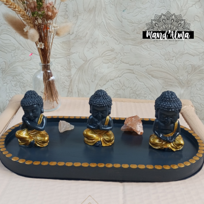 Três estatuetas de Buda em preto e dourado numa bandeja preta com cristais e vaso com flores secas