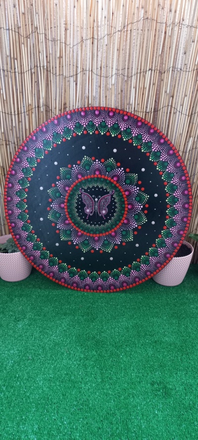 Roda decorativa pintada com borboleta ao centro e padrão colorido, encostada numa parede de bambu