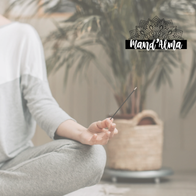Pessoa meditando segurando incenso com planta ao fundo e logo Mand'Alma