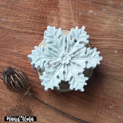 Ornamento branco em forma de floco de neve sobre superfície de madeira com flor seca ao lado