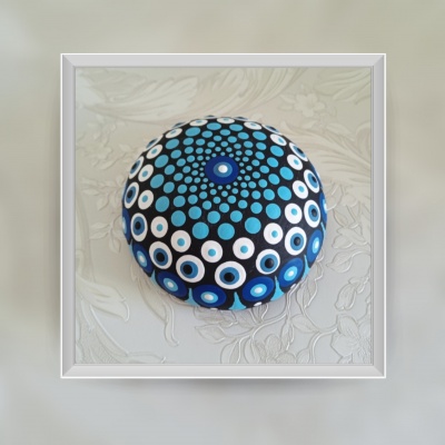 Pedra pintada redonda com padrão de círculos azuis, brancos e pretos sobre superfície floral clara