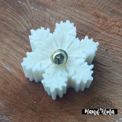 Sabonete branco em forma de floco de neve com enfeite metálico no centro numa superfície de madeira