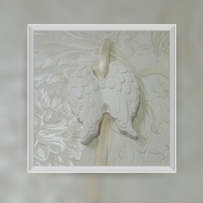 Decoração branca em forma de asas de anjo pendurada com fita bege sobre papel de parede floral creme.