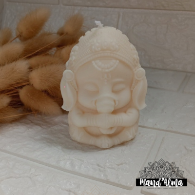 Vela branca em forma de Ganesha em superfície de ladrilhos com flores secas e logotipo Mand'Alma