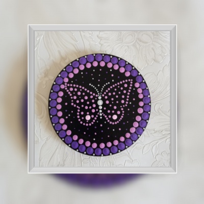 Disco decorativo redondo com padrão de borboleta em tons de roxo e lilás, em moldura branca sobre fundo branco texturizado.