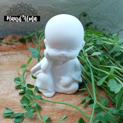 Figura decorativa branca de pequeno monge em pose pensativa numa superfície de madeira com folhas verdes ao redor