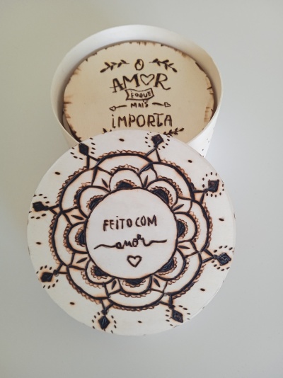 Caixa redonda branca decorada com padrão floral e texto escrito à mão em português.