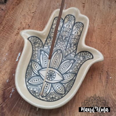 Incensário em cerâmica em forma de mão com desenho de olho e padrões florais, com incenso aceso, em madeira