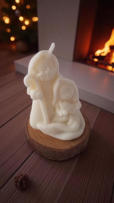 Vela branca esculpida de Natal sobre base de madeira com lareira e luzes ao fundo