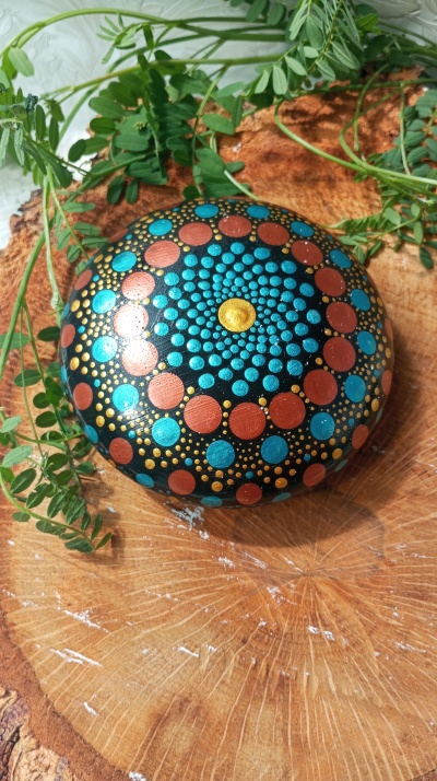 Pedra pintada com padrão colorido sobre madeira com folhas verdes