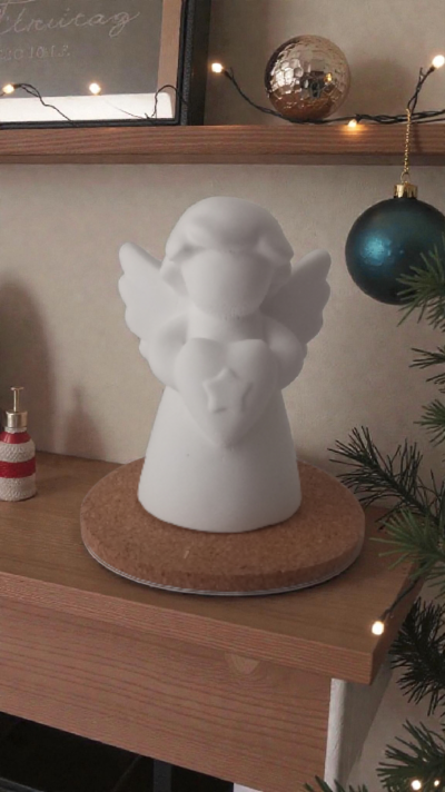 Estatueta branca de anjo com coração numa base de cortiça em mesa de madeira com decoração natalícia.