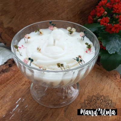 copo de vidro com sobremesa branca e flores secas sobre mesa de madeira com planta vermelha ao fundo