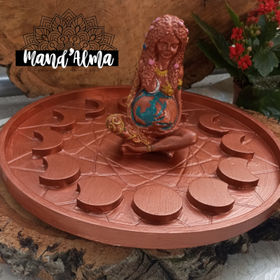 Tabuleiro decorativo castanho com figura feminina segurando esfera azul no centro, sobre base de madeira e plantas com flores vermelhas ao fundo.