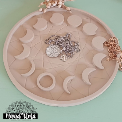 Prato decorativo redondo com fases da lua em relevo e colares de metal sobre superfície verde