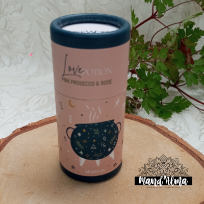 Embalagem cilíndrica cor-de-rosa de óleo aromático Love Potion com ilustração de caneca azul e tampa azul escura sobre superfície de madeira