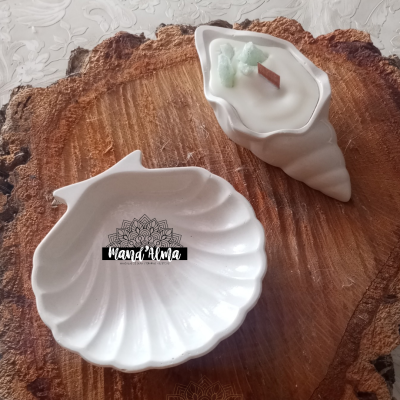 Dois objetos decorativos de cerâmica branca em formato de conchas, um com vela e pau de madeira, sobre madeira rústica