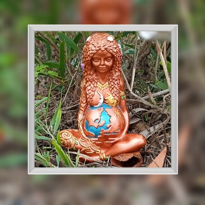 Estátua de mulher grávida em cobre com detalhes coloridos, sentada na vegetação