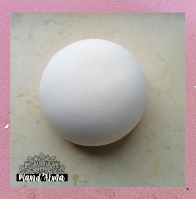 Esfera branca sobre superfície bege com texto 'Mamá Alma' e desenho ornamental