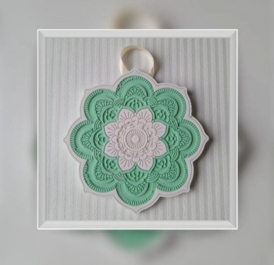 Mandala decorativa verde água e branca pendurada numa parede cinza claro com padrão listrado